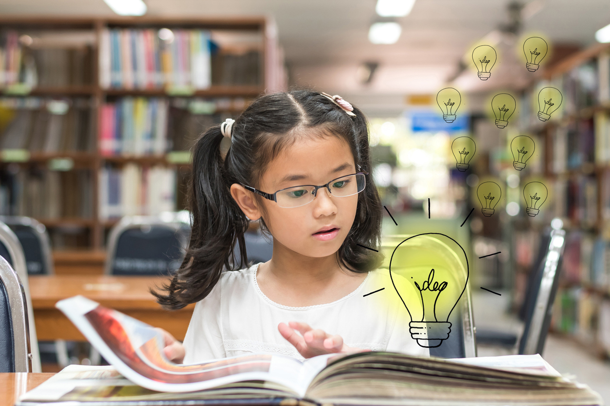 kid surprised reading book with lightbulb in library