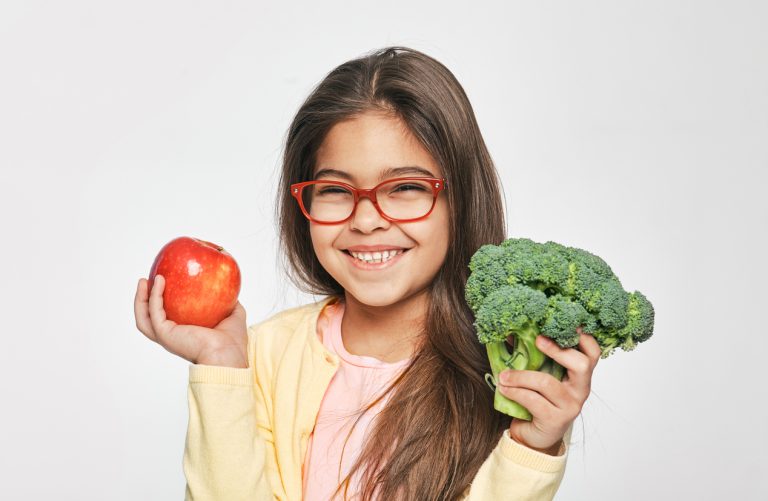 Smiling mixed race girl holding an apple and broccoli in her hands. Healthy vegetarian food for kids