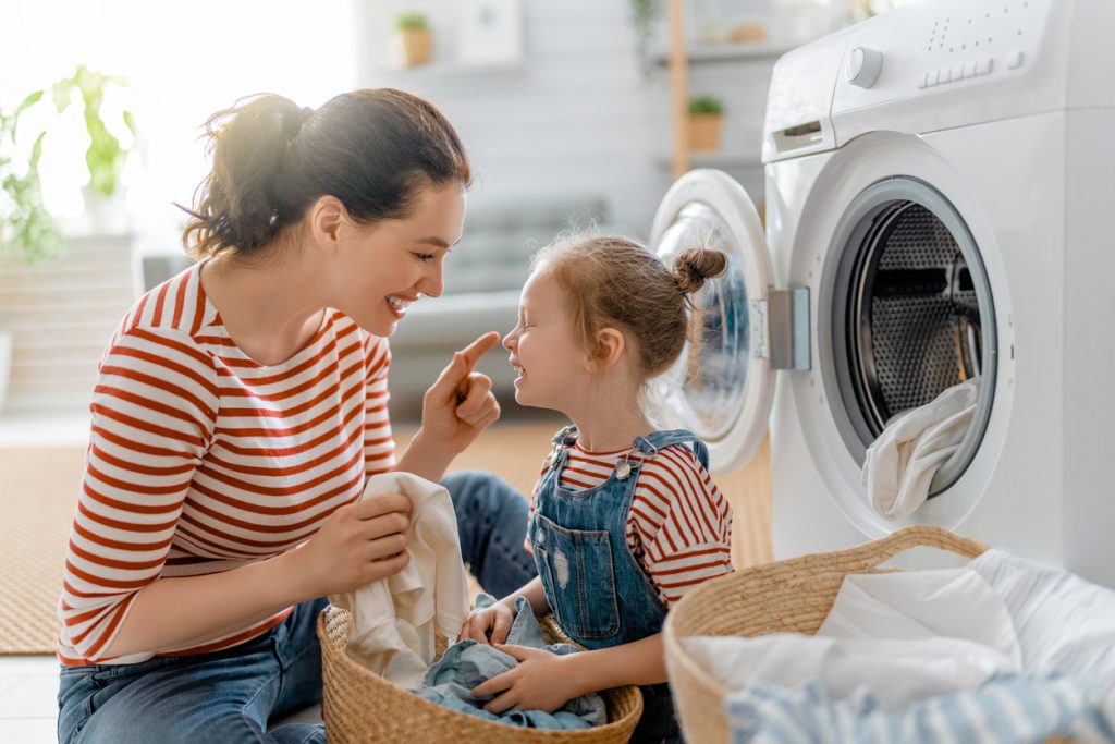 Beautiful young woman and child girl little helper are having fun and smiling while doing laundry at home.