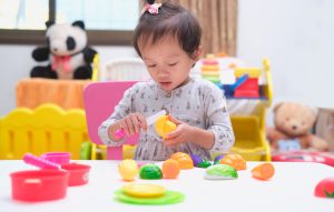Cute little Asian toddler baby girl child having fun playing alone with cooking toys, Slice and play velcro vegetable cutting set, Pretend and role play toys for kid