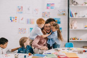 kids hugging happy teacher at table in classroom