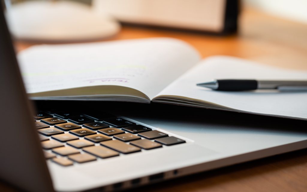 Laptop Computer on a Modern Wooden Business Desk with a Notepad and Pen in Unfocused Background.